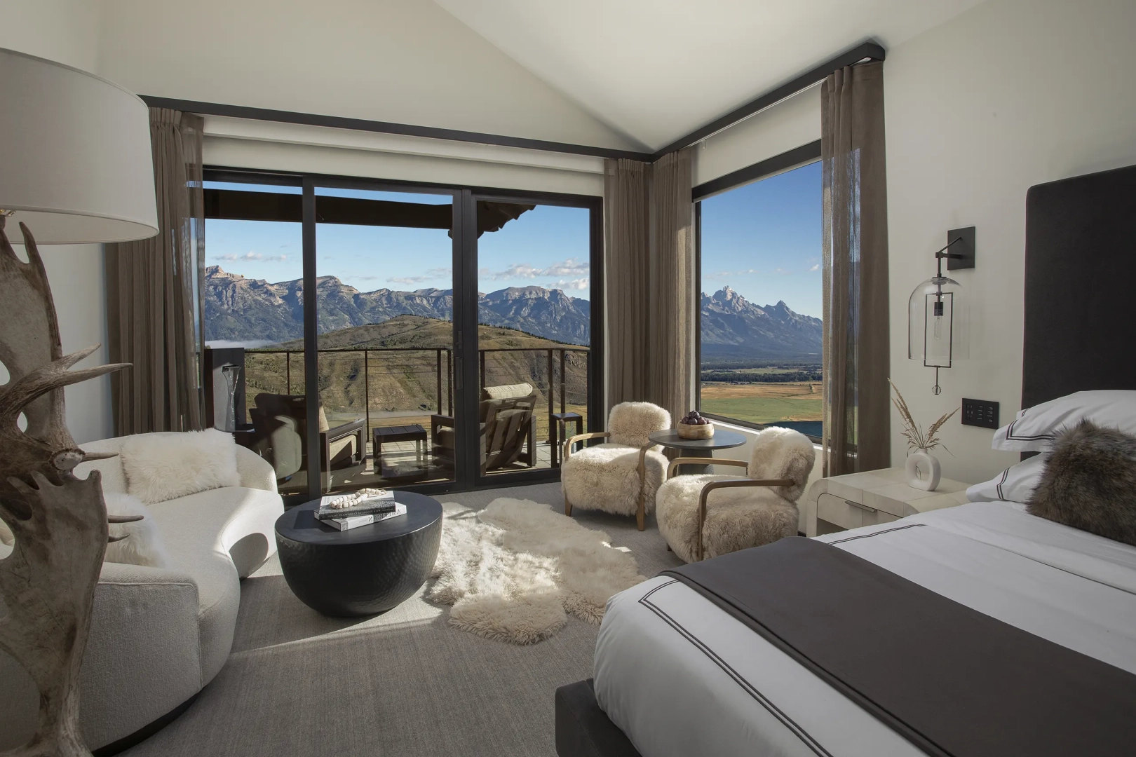 A luxurious room with a couch, two chairs, a table, and bed overlooking the Wyoming landscape.